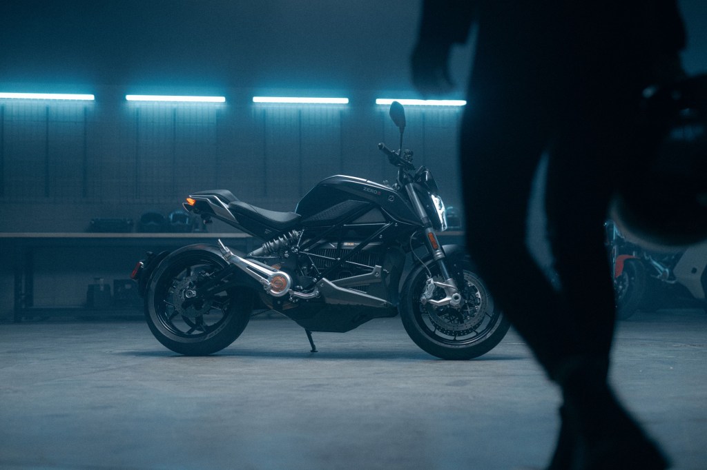 The side view of a black 2022 Zero SR in a garage with a rider approaching
