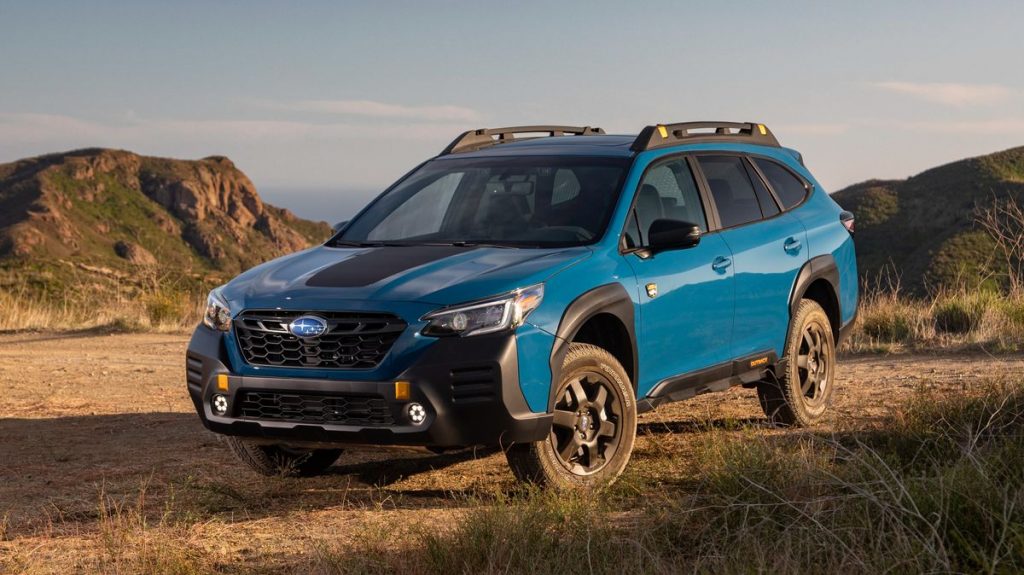 Blue 2022 Subaru Outback Wilderness parked in dirt with a mountainous background, it's one of the best commuter SUVs, according to KBB.
