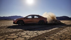 An orange non-JDM 2022 Subaru WRX sports sedan mid-drift on a desert lakebed