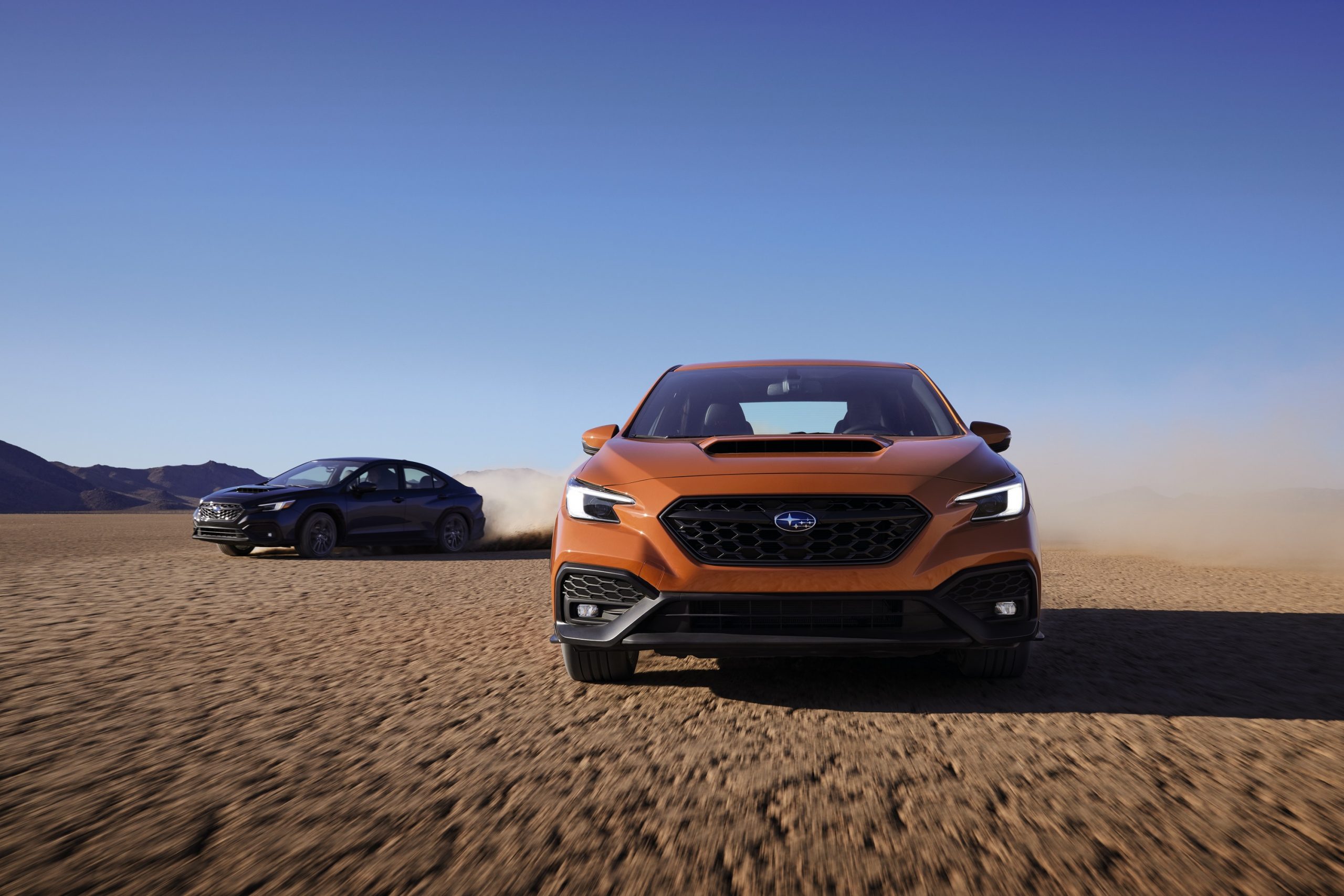 A front shot of a Subaru WRX driving across a dry lakebed, with another model close behind