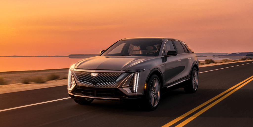 The 2023 Cadillac Lyriq electric luxury SUV driving on a highway near the sea as the sun sets
