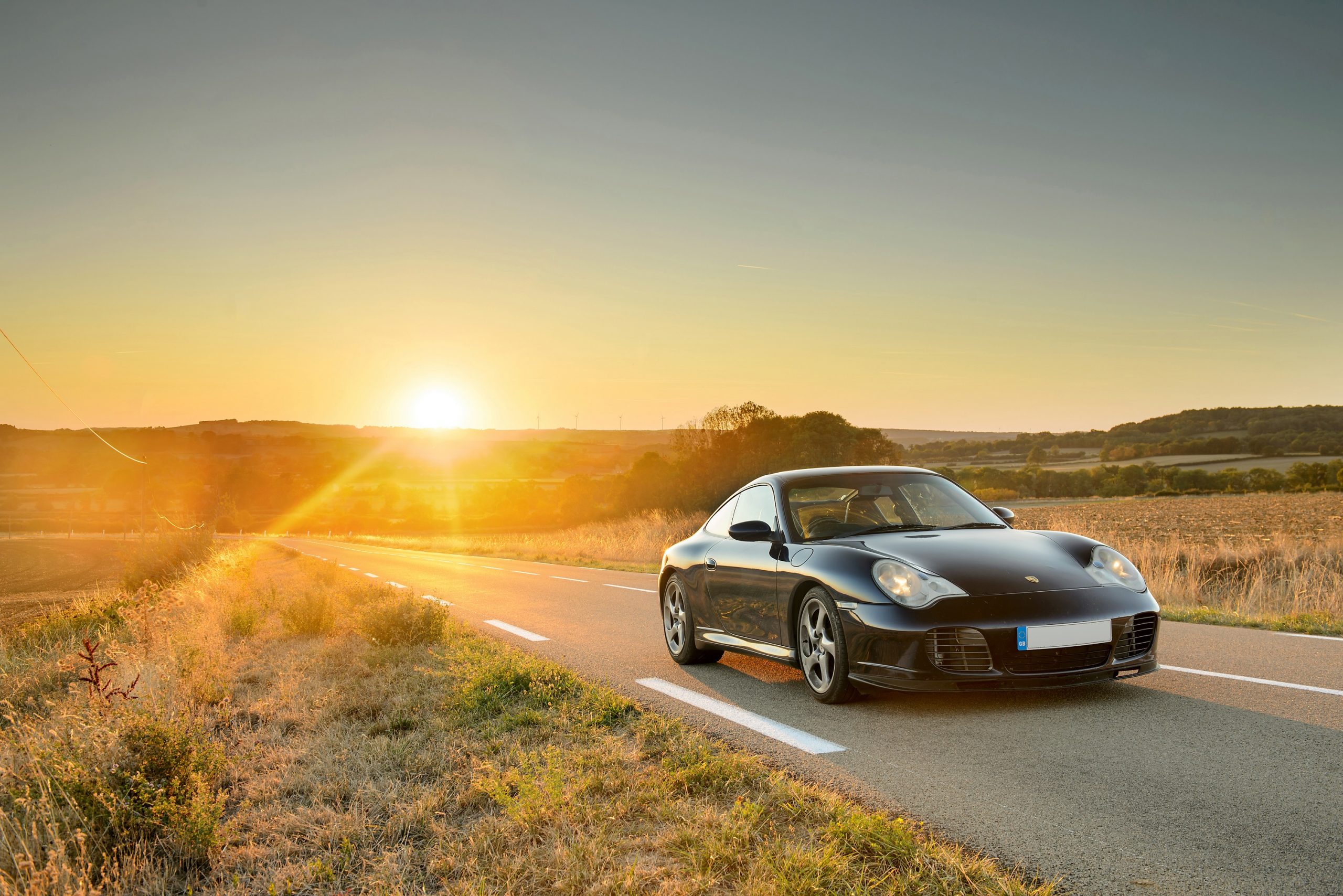 A black 996 generation 911 shot from the front at sunset on a country road