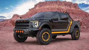 A 2022 Ford F-150 Raptor in a dark grey color with a light grey and yellow racing stripe graphics. The truck is lifted with off road wheels and tires. The wheels have bead locks that are yellow and color matched to the graphics. This truck will be on display at SEMA 2021