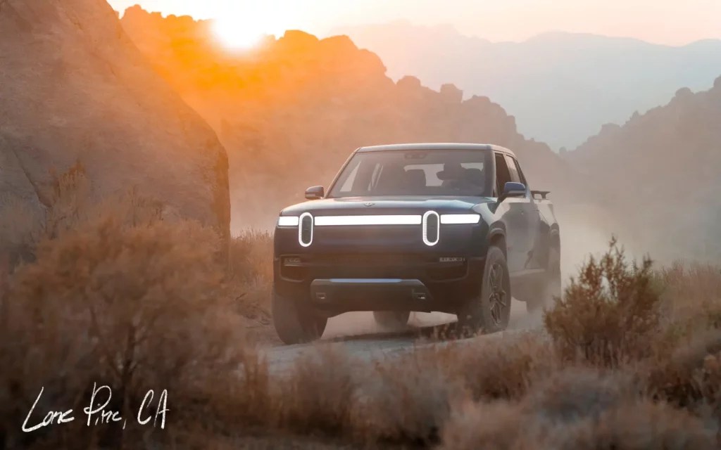 Blue Rivian R1T driving by a large rock
