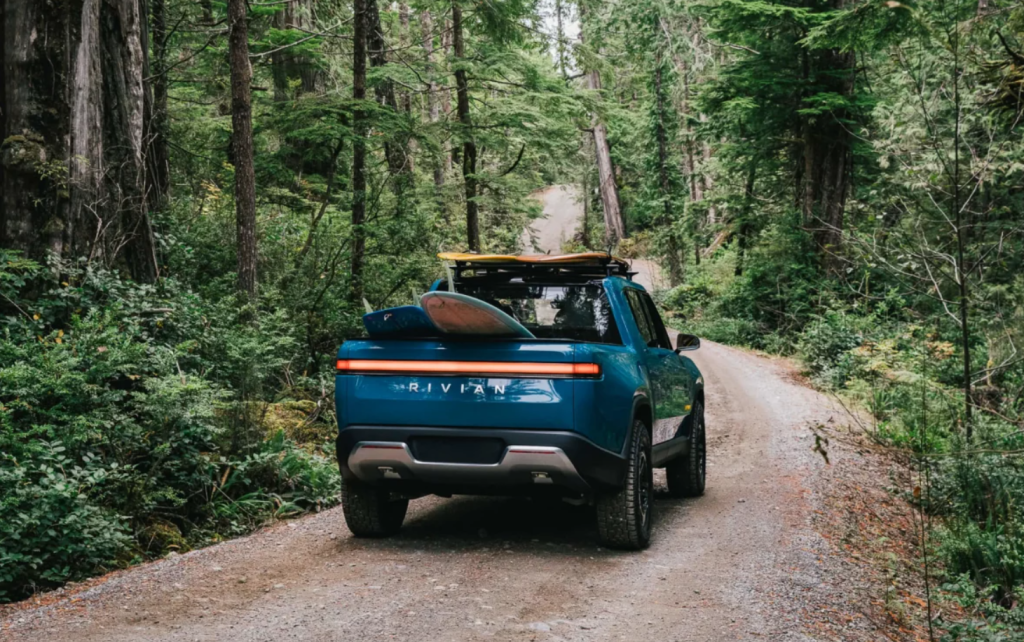 Blue Rivian R1T driving on a forest road, do electric pickup trucks have a good driving range compared to Tesla models?