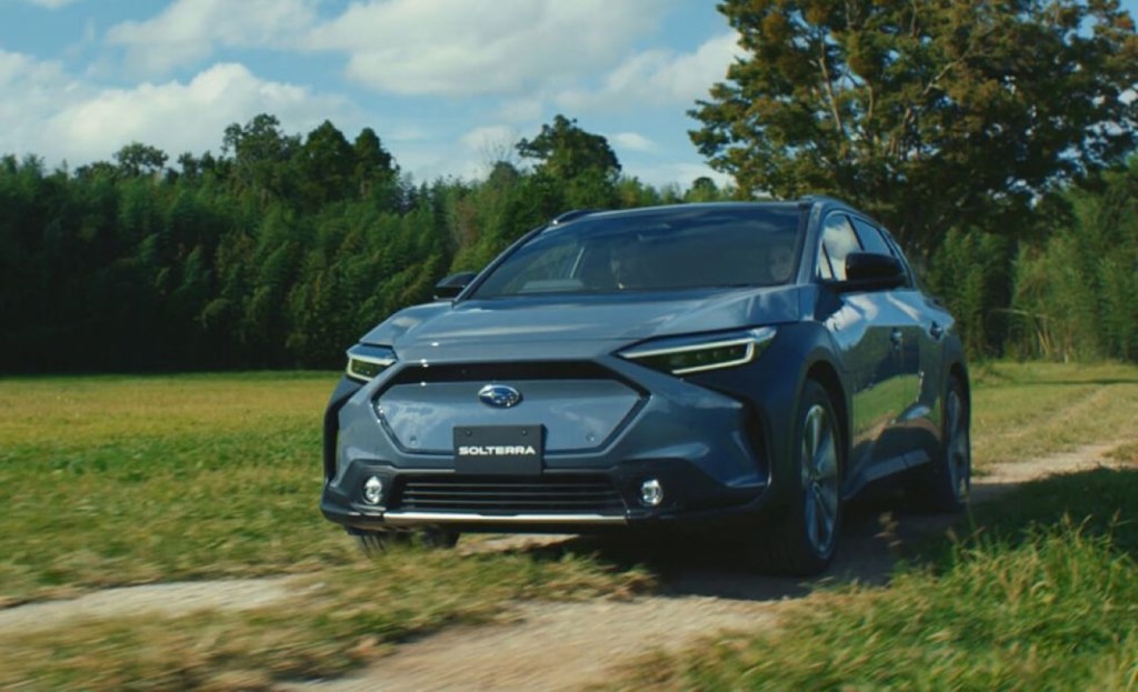 Blue-green 2023 Subaru Solterra crossover EV driving through a field, showing the horsepower and acceleration specs from its electric motors