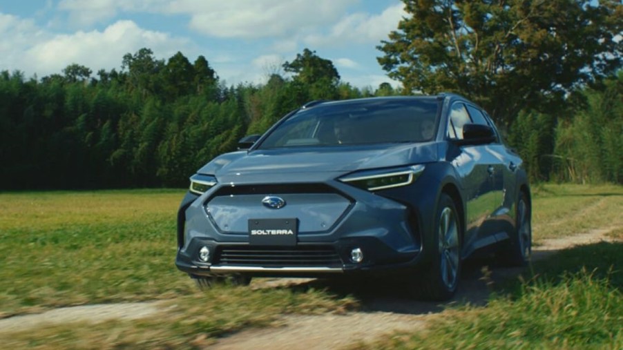 Blue-green 2023 Subaru Solterra crossover EV driving through a field, showing the horsepower and acceleration specs from its electric motors