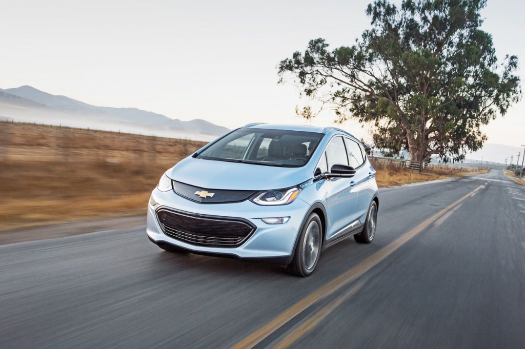 A 2017 Chevy bolt in light blue driving down a road toward the camera. GM recently announced an assembly plant would be closed for three weeks due to the nationwide Chevy Bolt recall
