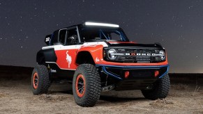 A red and black SEMA Show Ford Bronco Desert Racer parked in a desert at night.