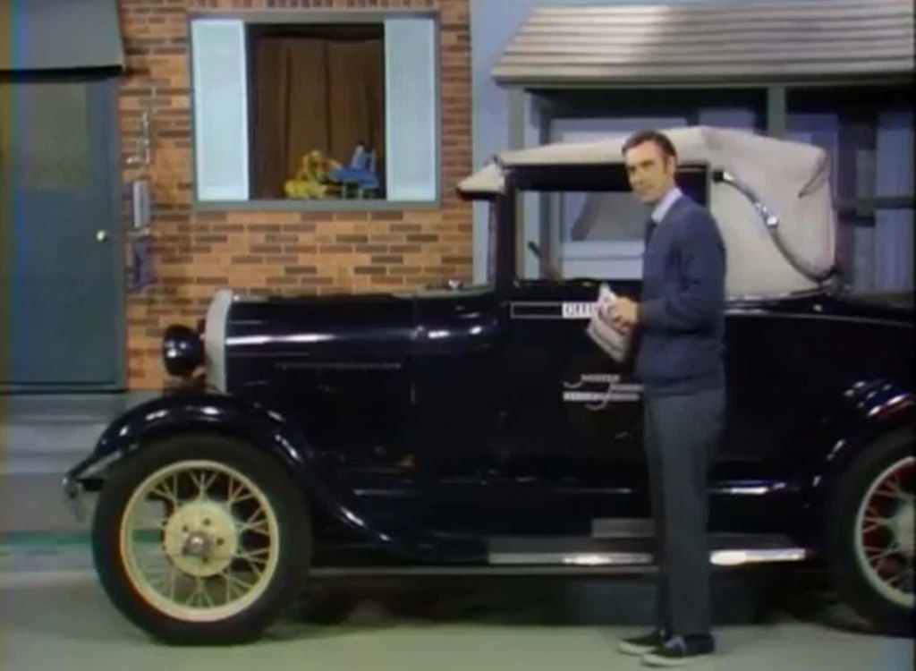 Fred Rogers standing next to a navy blue 1928 Ford Model A Sport Coupe classic car in Mister Rogers' Neighborhood