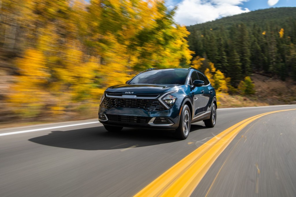 Front view of blue 2023 Kia Sportage Hybrid driving by a forest