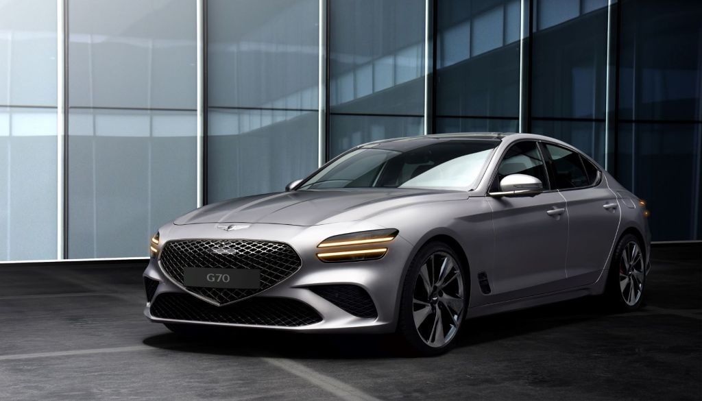 The Genesis G70 luxury executive compact sedan with a gray silver paint color option parked outside a building of glass panels