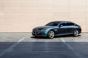 The Genesis G80 luxury executive sedan with a blue paint color option parked near a wall of beige tiles