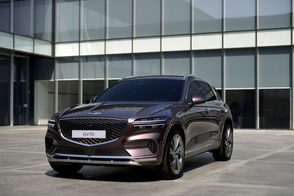 The Genesis GV70 luxury compact crossover SUV with a dark red paint color option parked on a building's entrance plaza