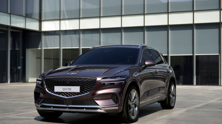 The Genesis GV70 luxury compact crossover SUV with a dark red paint color option parked on a building's entrance plaza