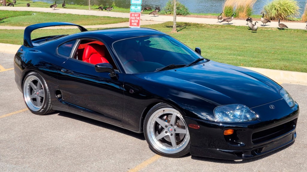 A black JDM 1994 Toyota Supra Mk4 Turbo in a parking lot next to a lake with some geese