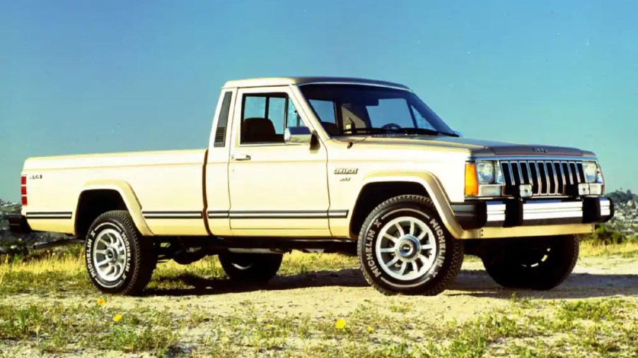 A silver-and-gold Jeep 'MJ' Comanche parked on a sandy grassy hill