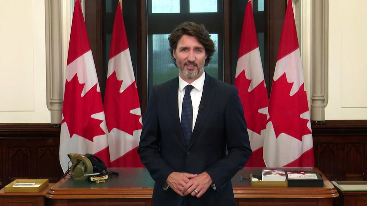 Canadian Prime Minister Justin Trudeau standing in his office with a row of four Canadian flags behind him.