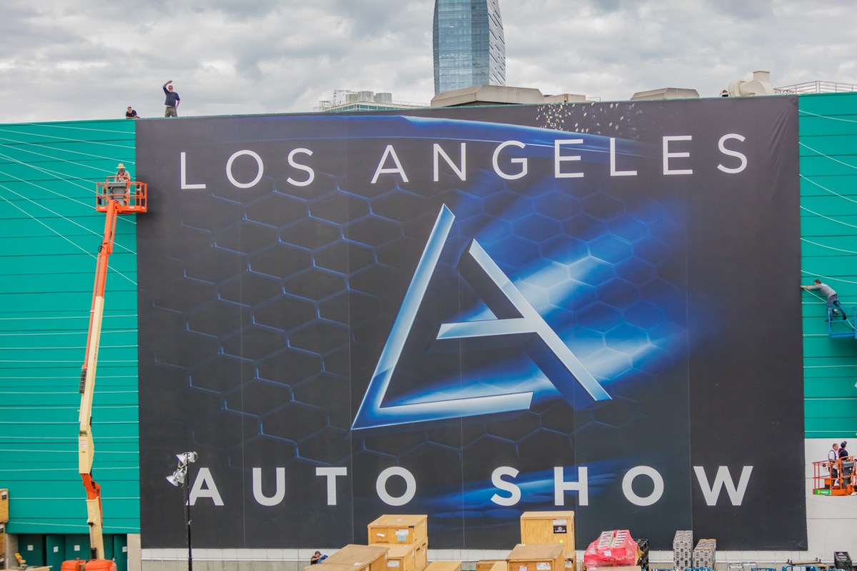 A massive vinyl sign for the LA Auto Show being hoisted onto the LA Convention Center