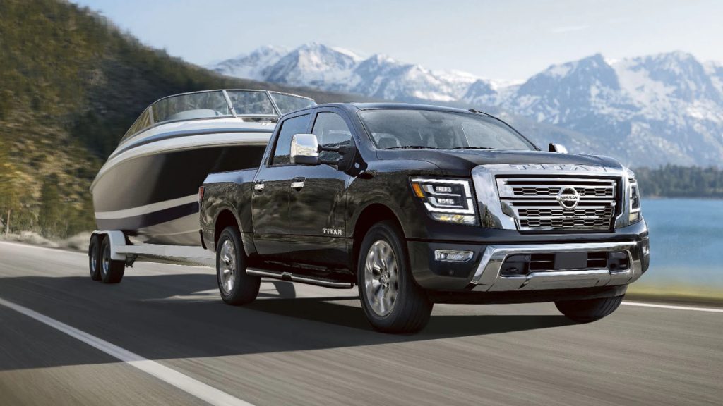 A black Nissan Titan pulls a boat down the highway with a mountain background