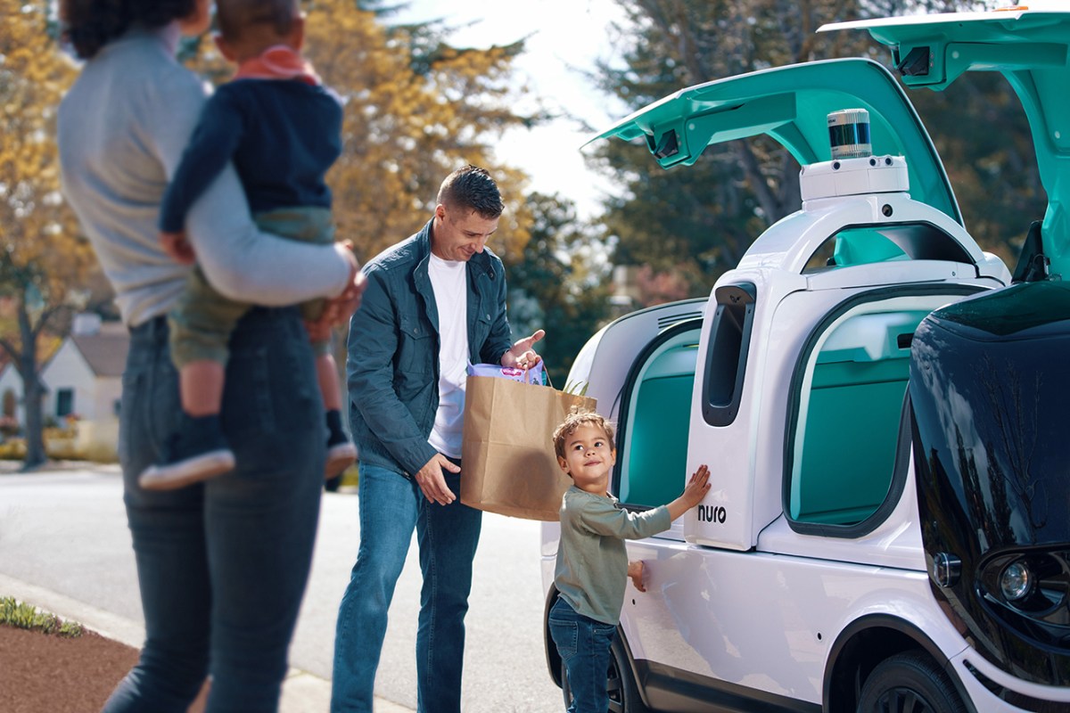 A family taking its items from a Nuro R2 autonomous delivery vehicle. Nuro specializes in small autonomous vehicles that can deliver consumer goods such as groceries, prescription drugs, and hot food.