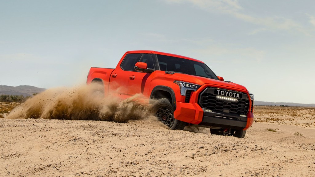 Orange-red 2022 Toyota Tundra driving on sandy terrain, it'll have over 100 accessories available for prime customization. 