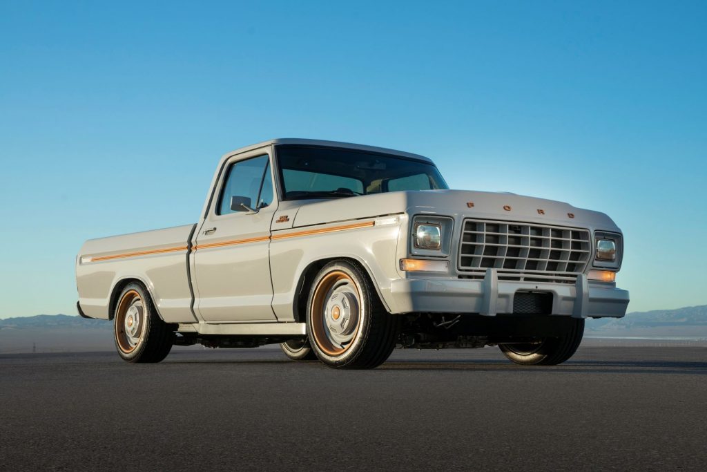Passenger's side front angle view of grey and orange Ford F-100 EV pickup truck at SEMA 2021.