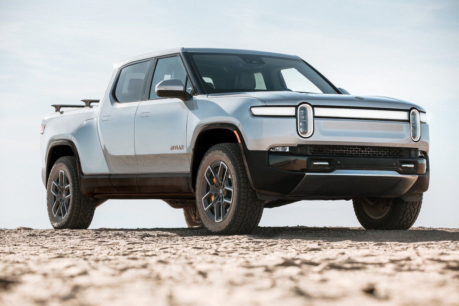 Passenger's side front angle view of silver Rivian R1T in a comparison between the Rivian R1S