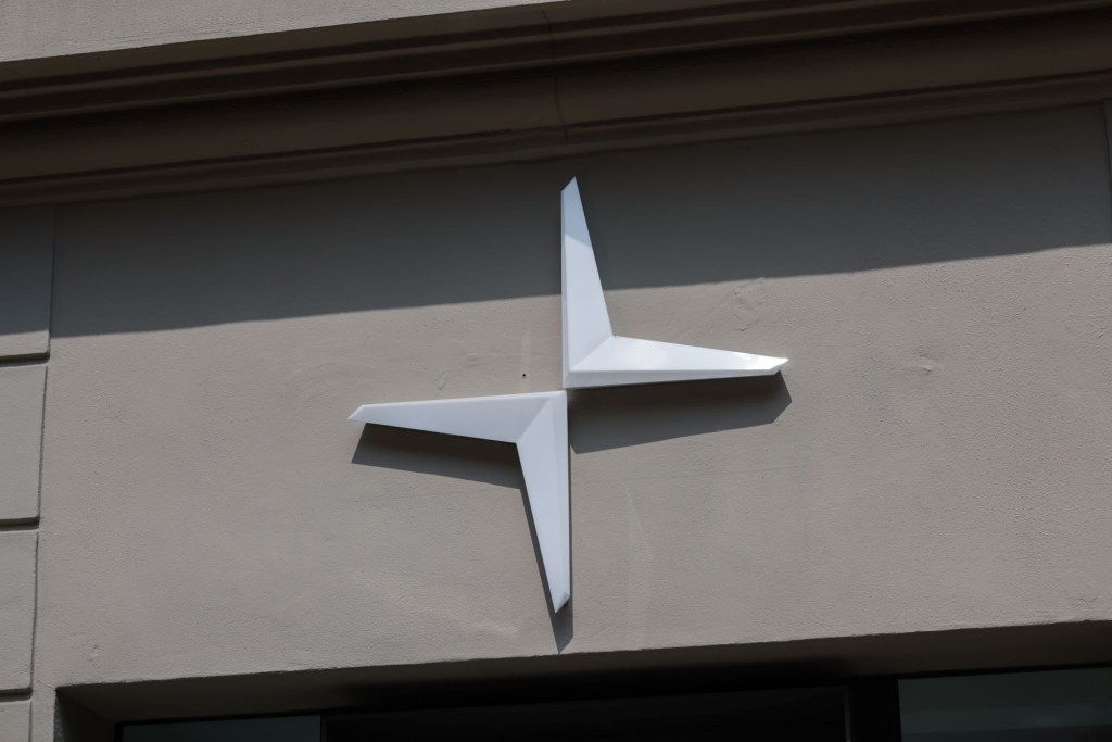 A silver Polestar logo on the side of a tan building.