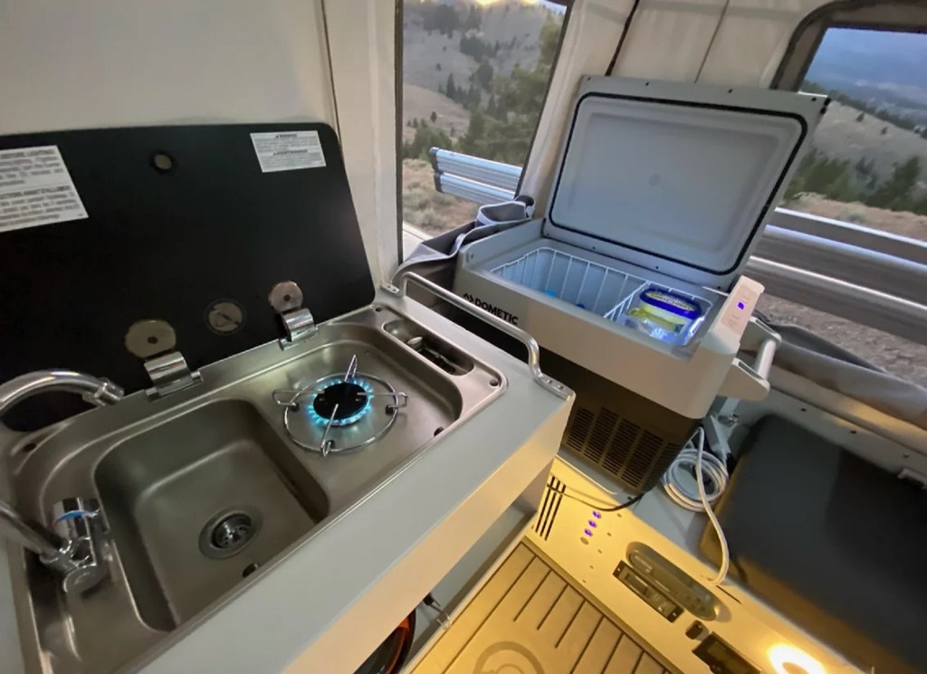 The stainless-steel sink, fridge, and cooktop area of a Skinny Guy Campers Kit 'N Kaboodle