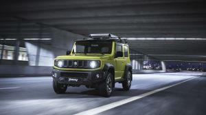 The fourth-generation Suzuki Jimny off-road mini SUV with a green paint color option driving under a bridge at night