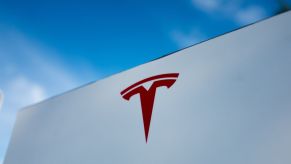 A red Tesla logo on a white building with a blue sky.