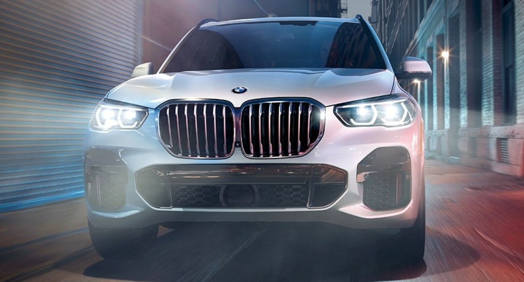 A white 2022 BMW X5 is driving down an alleyway at night. 