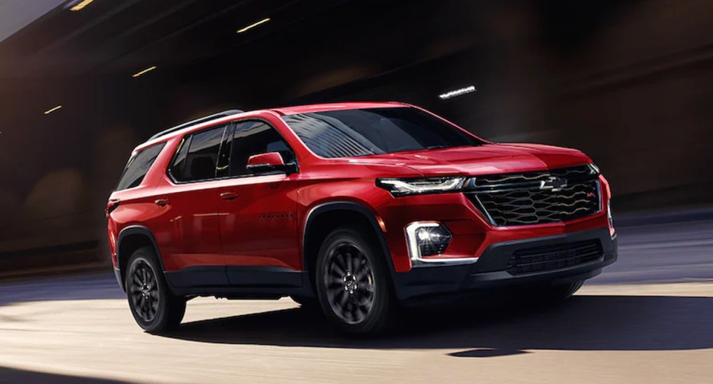A red Chevrolet Traverse is driving on the road. 