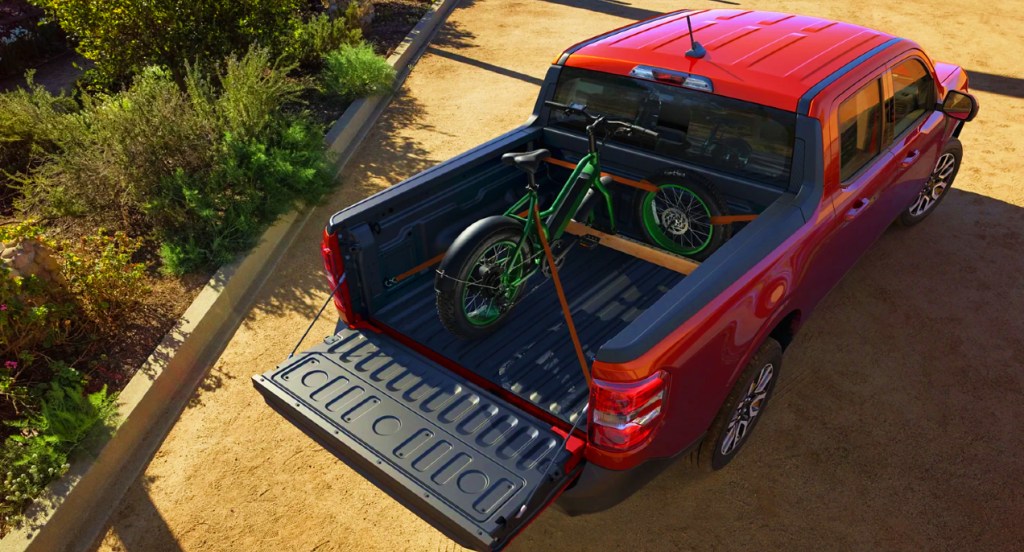 The trunk of a red 2022 Ford Maverick is holding a green bicycle. 