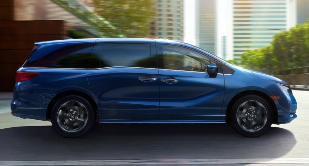 A blue Honda Odyssey minivan is driving down the road. 