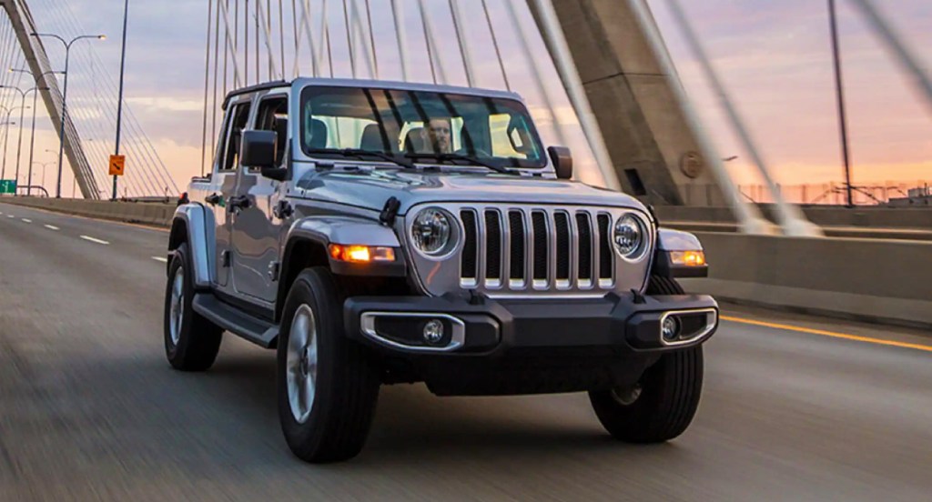 A gray Jeep Wrangler is driving on a bridge. 