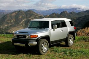 The Toyota FJ Cruiser retro-style midsize SUV with a gray silver body and a white roof parked on top of a grassy hill with mountains in the background