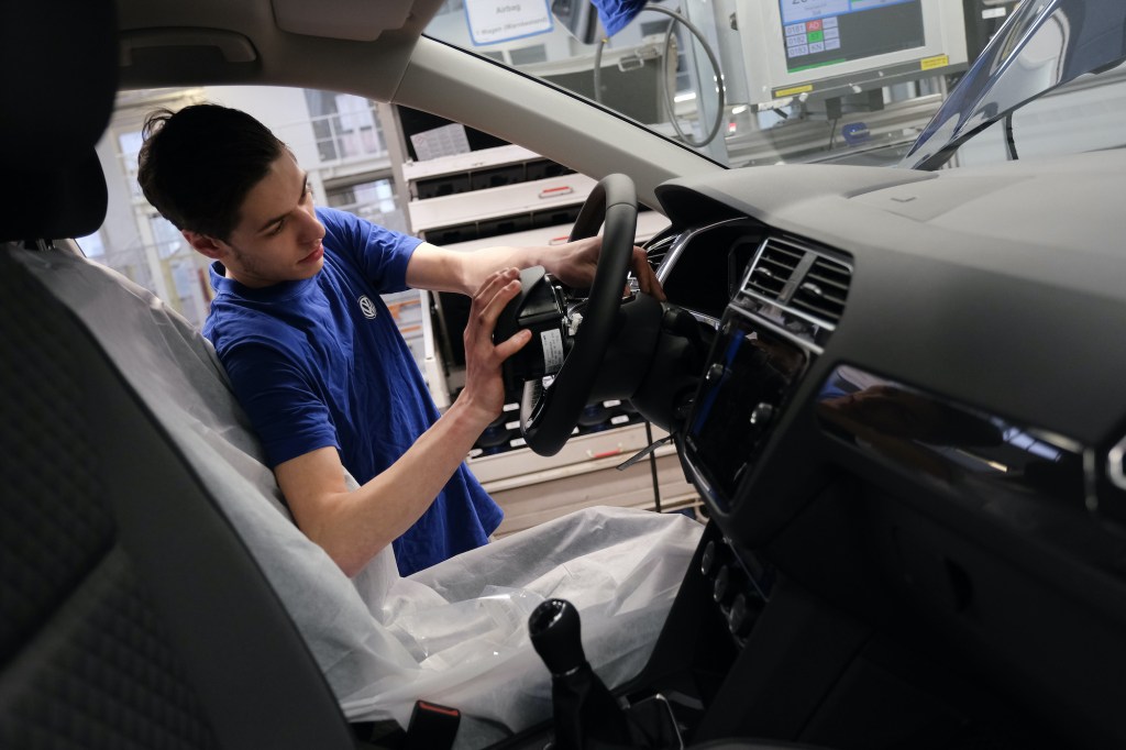 A worker installs an airbag into the steering wheel of a car on the assembly line for Volkswagen Touareg, Touran, and T-Roc models at the Volkswagen factory
