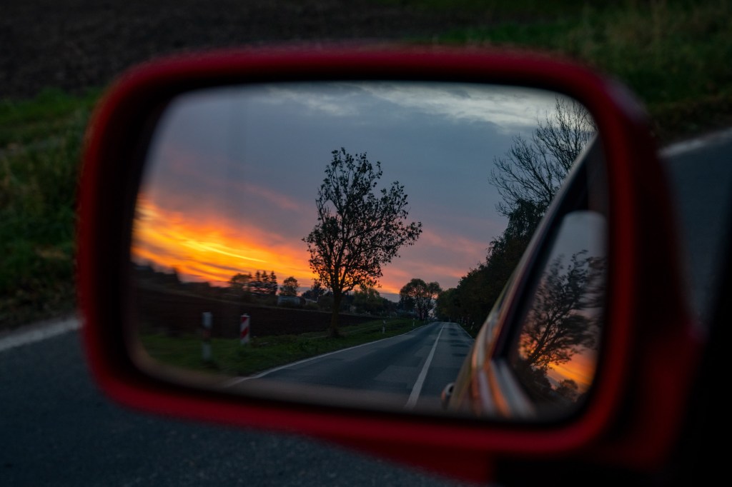 The setting sun on the horizon is reflected in the wing mirror of a car.