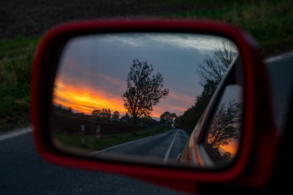 The setting sun on the horizon is reflected in the wing mirror of a car. 