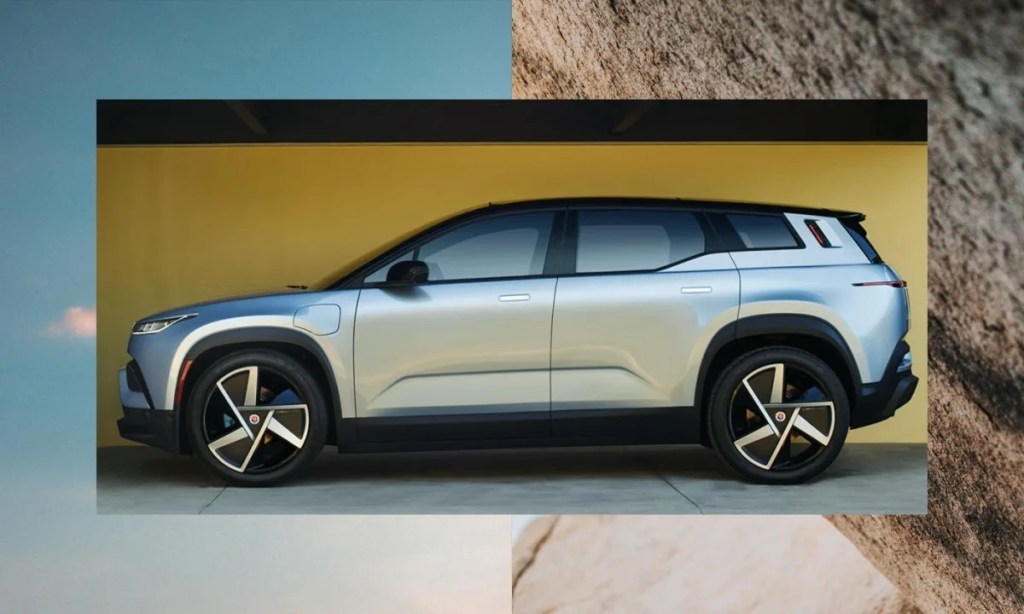 A silver Fisker Ocean SUV outside of a yellow background.