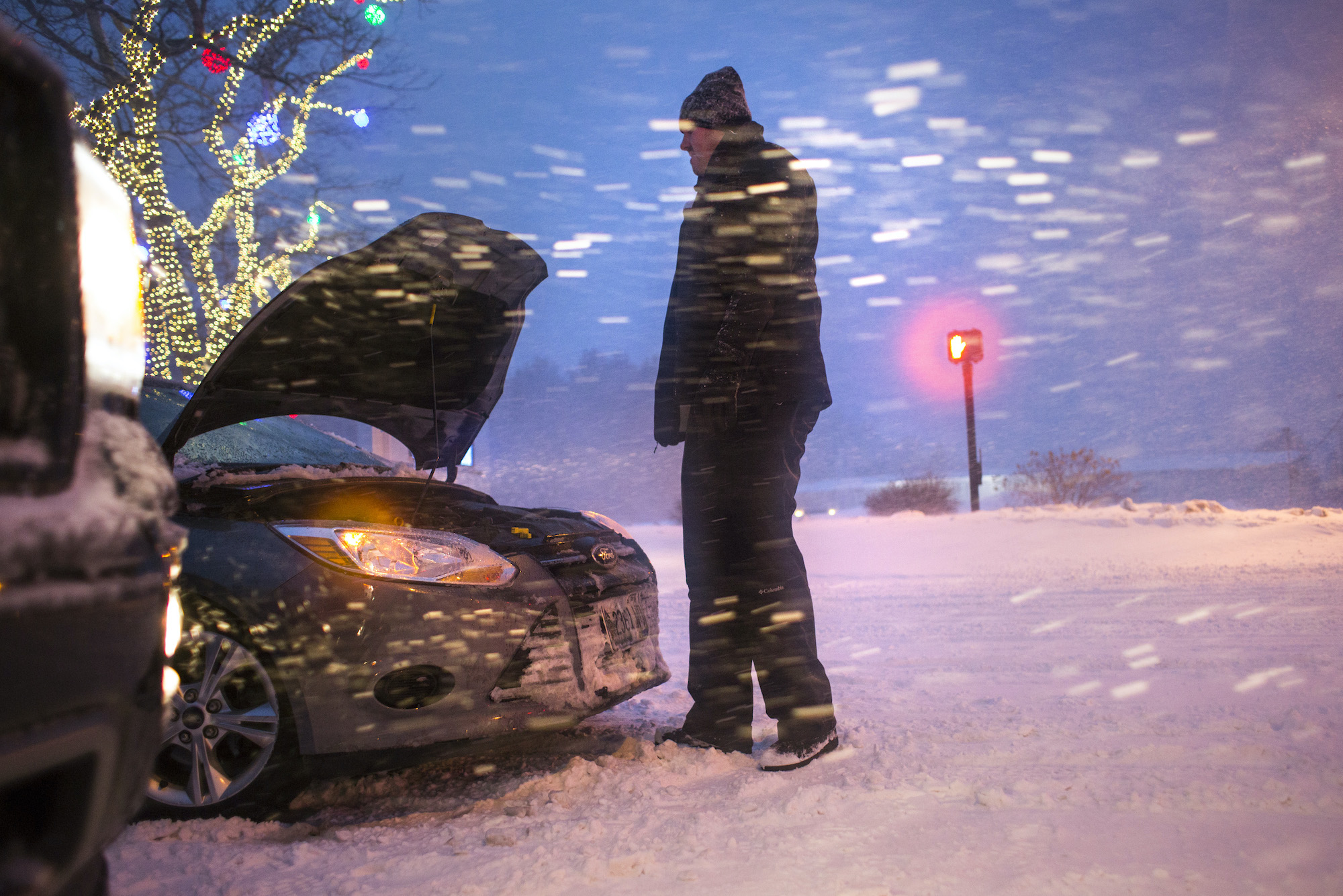 Man stands outside of a stranded car in the snow