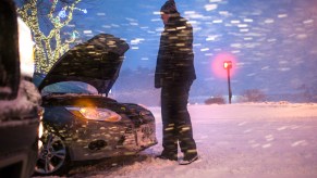 Man stands outside of a stranded car in the snow