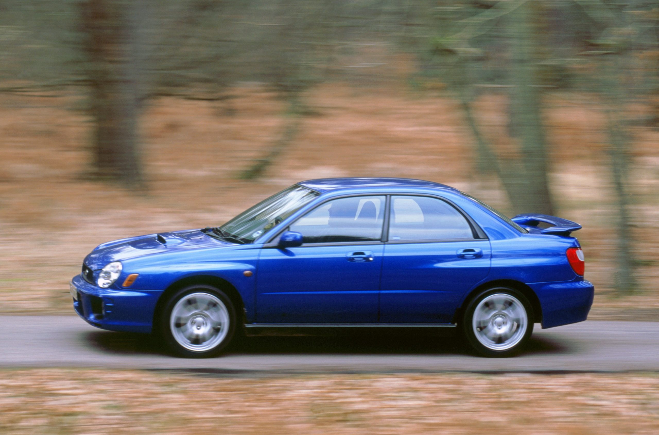 A 2001 Subaru WRX shot in profile flying down a country road