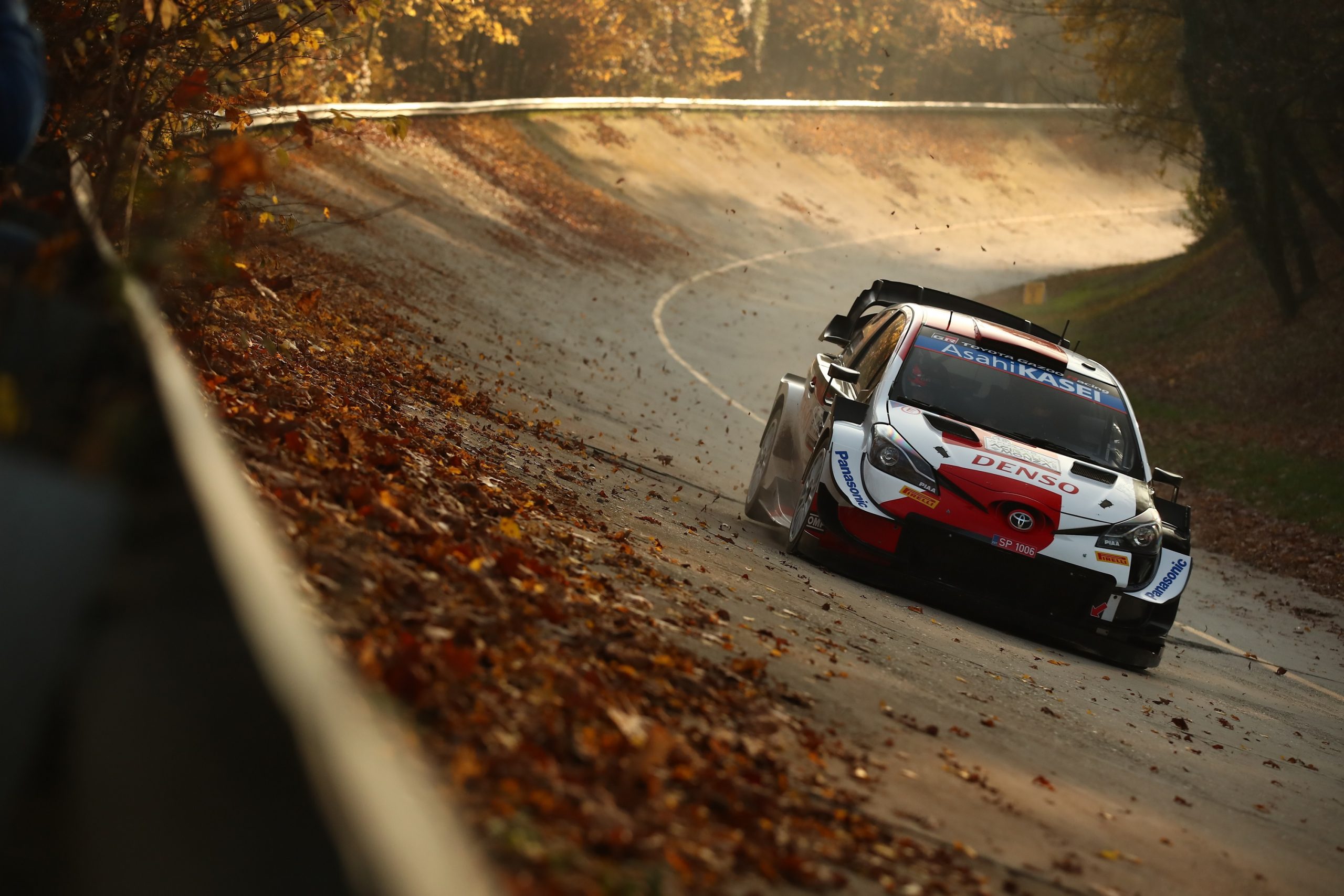 A red and white Gazoo Racing Toyota Yaris rally car shot from the front on an oval circuit