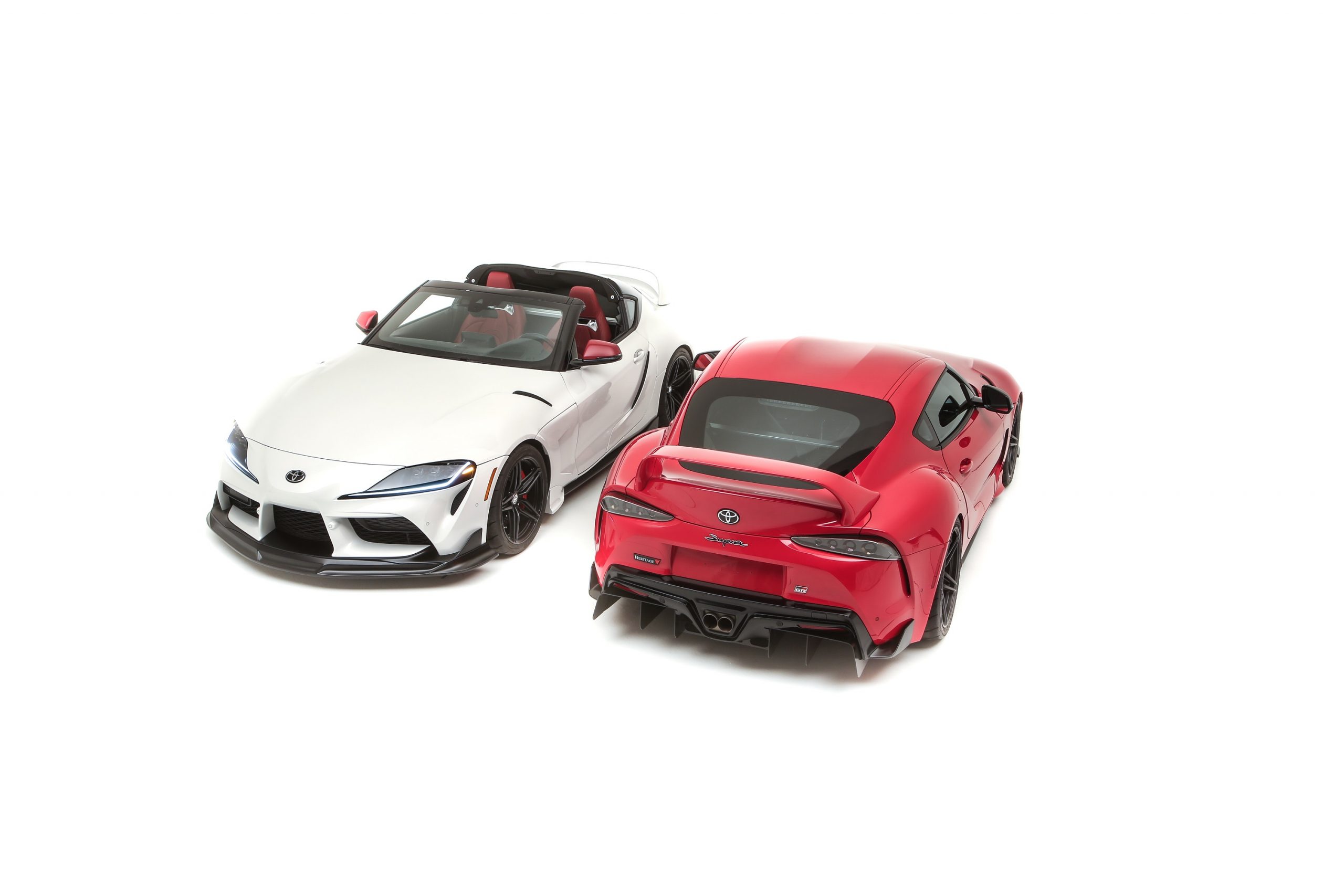 The front and rear of two new Toyota Supra Heritage models in white and red respectively, one a targa and one a coupe