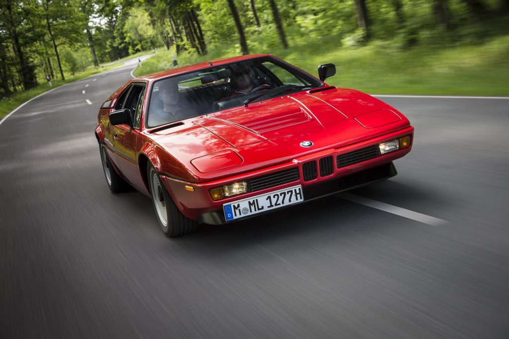 A red 1978-1981 BMW M1 driving down a forest road