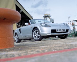 A silver 2000 Toyota MR2 convertible parked in a shipyard