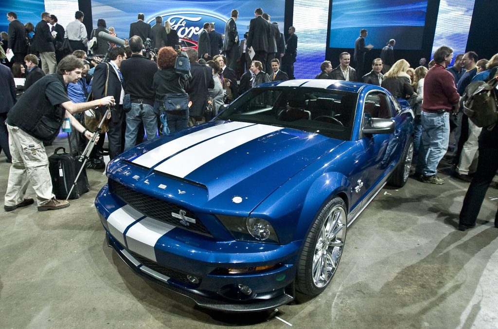 A blue-with-white-stripes 2008 Ford Mustang Shelby GT500KR at NAIAS surrounded by photographers